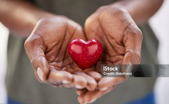 Hands holding a small figurine of a red heart